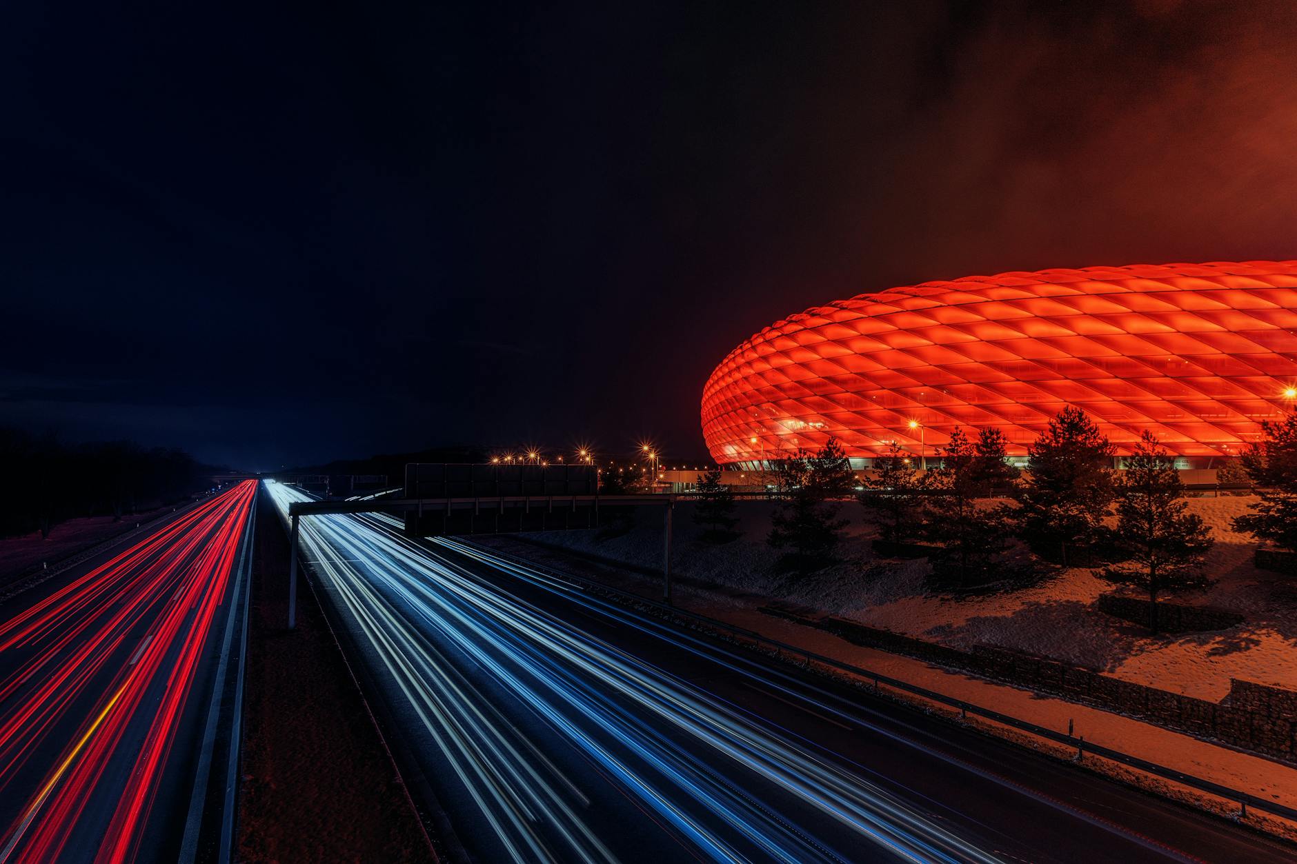 Allianz Arena nocą oświetlona kolorami, z dynamicznymi smugami świateł