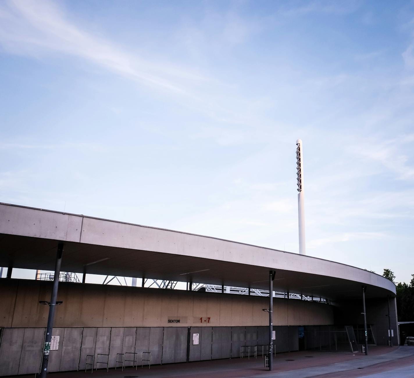 Najciekawsze rozwiązania wejść i bramek na nowoczesnych stadionach Nowoczesna fasada stadionu piłkarskiego na tle błękitnego nieba
