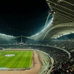 Największe stadiony w Polsce: ranking pojemności Pełne trybuny piłkarskiego stadionu nocą w blasku jupiterów