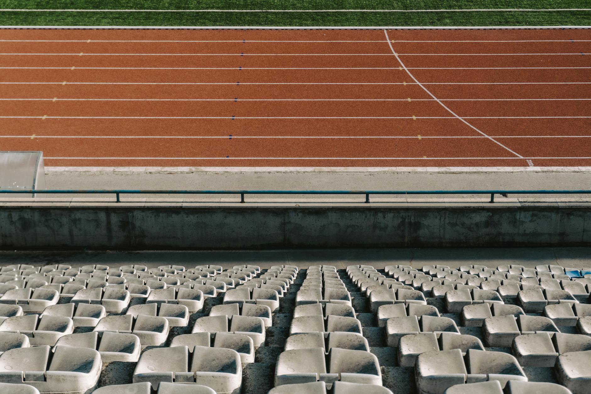 Puste rzędy stadionowych krzesełek z widokiem na bieżnię lekkoatletyczną