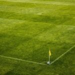 Od betonu do zieleni: jak wprowadza się rośliny na obiekty sportowe Róg zielonego boiska piłkarskiego z żółtą chorągiewką i piłką
