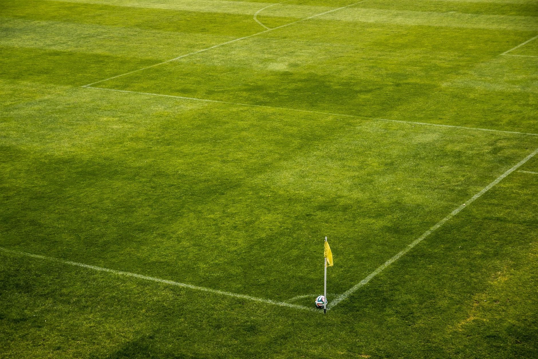 Od betonu do zieleni: jak wprowadza się rośliny na obiekty sportowe Róg zielonego boiska piłkarskiego z żółtą chorągiewką i piłką