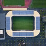 Zielone stadiony: panele PV, retencja i certyfikaty w nowych inwestycjach Nowoczesny stadion z panelami fotowoltaicznymi widziany z drona